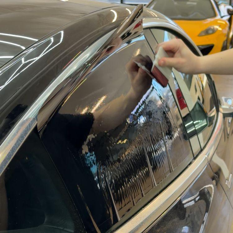 Installer applying window tint film to a car window using a squeegee tool