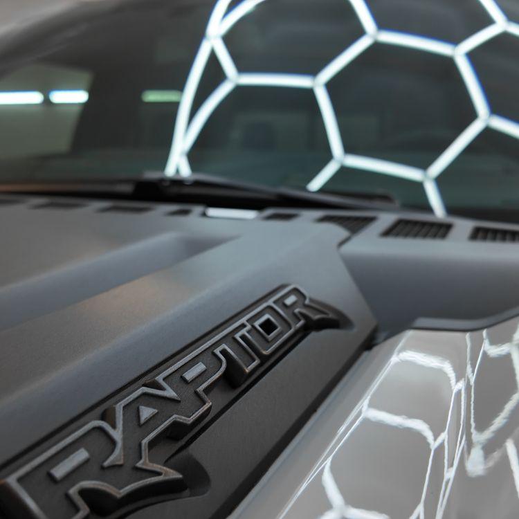 Close-up of Ford Raptor hood with honeycomb LED ceiling lights reflecting on clear paint protection film