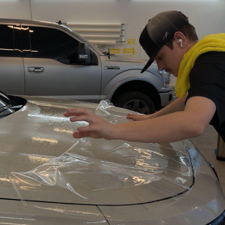Technician smoothing clear paint protection film onto the hood of a silver truck