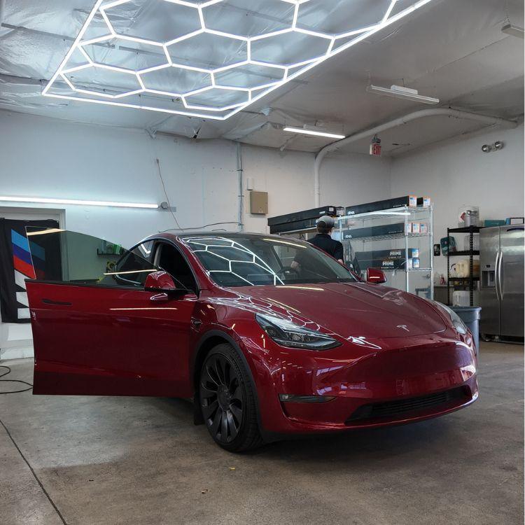 Red Tesla Model Y parked inside a modern auto detailing shop with hex ceiling lights