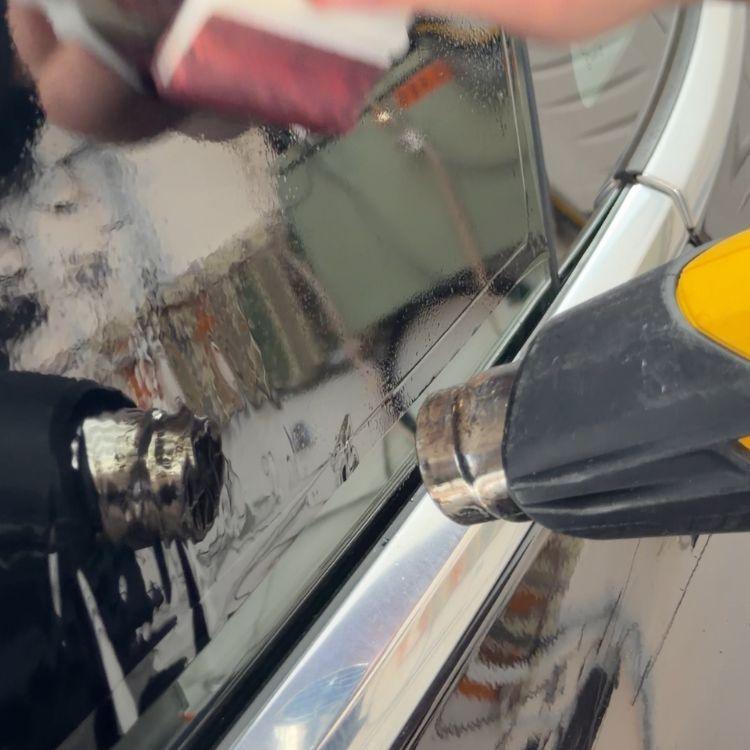 Technician using a heat gun to shrink and form window tint film onto a car window